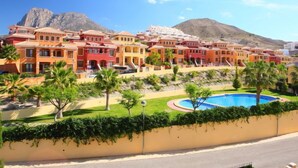 Un complejo turístico frente al mar con edificios de colores, una piscina y montañas al fondo.