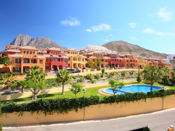 A coastal resort with colorful buildings, a swimming pool, and a mountain backdrop.