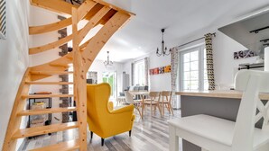 A modern interior with a wooden staircase, a yellow armchair, and a dining area with white chairs.