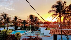 A pool area with a swing set, surrounded by palm trees and a sunset in the background. - Esplanada Hotel (Paraguacu Paulista)