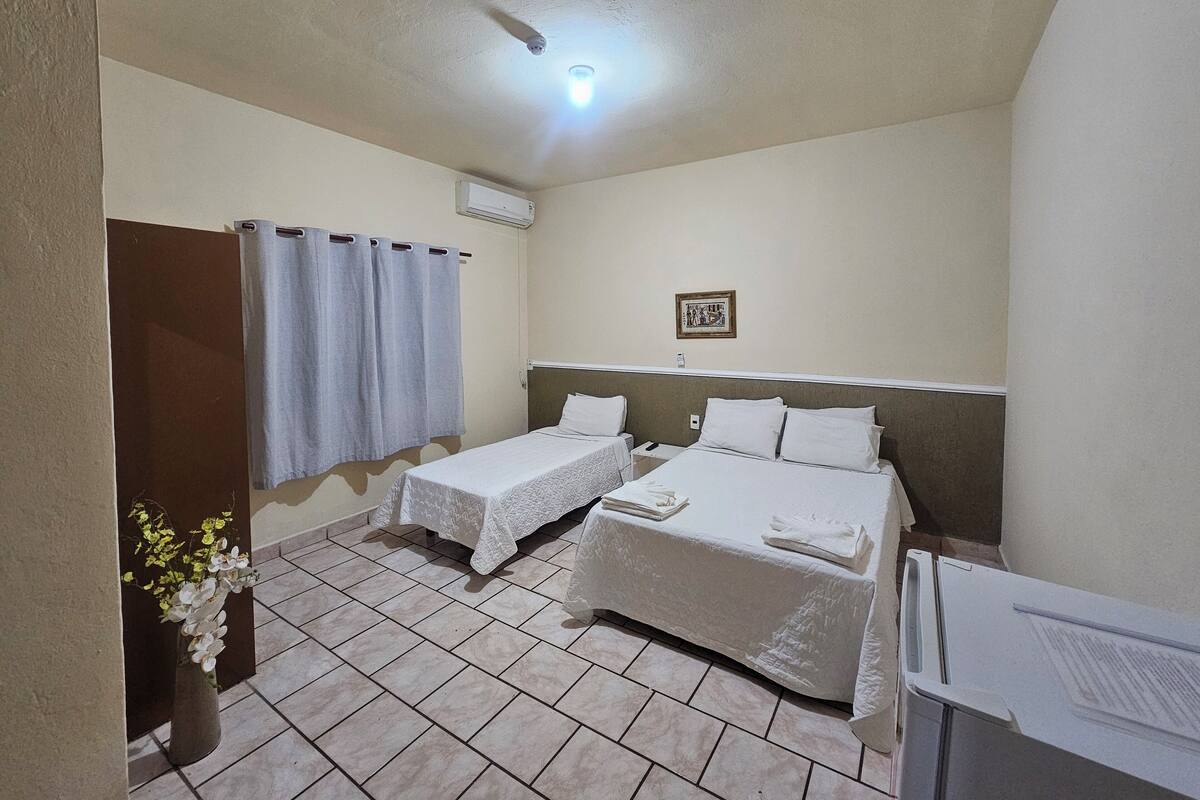 Une chambre d’hôtel avec deux lits simples, une petite table, une chaise, une plante en pot et un luminaire au plafond.
