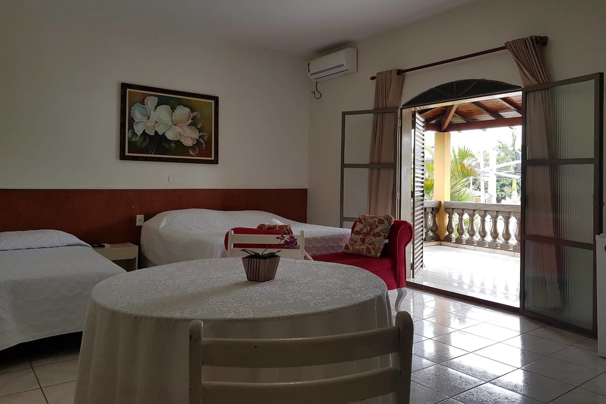 Une chambre d’hôtel avec deux lits, une table ronde, une chaise, un tableau, un appareil de climatisation et un balcon avec vue.