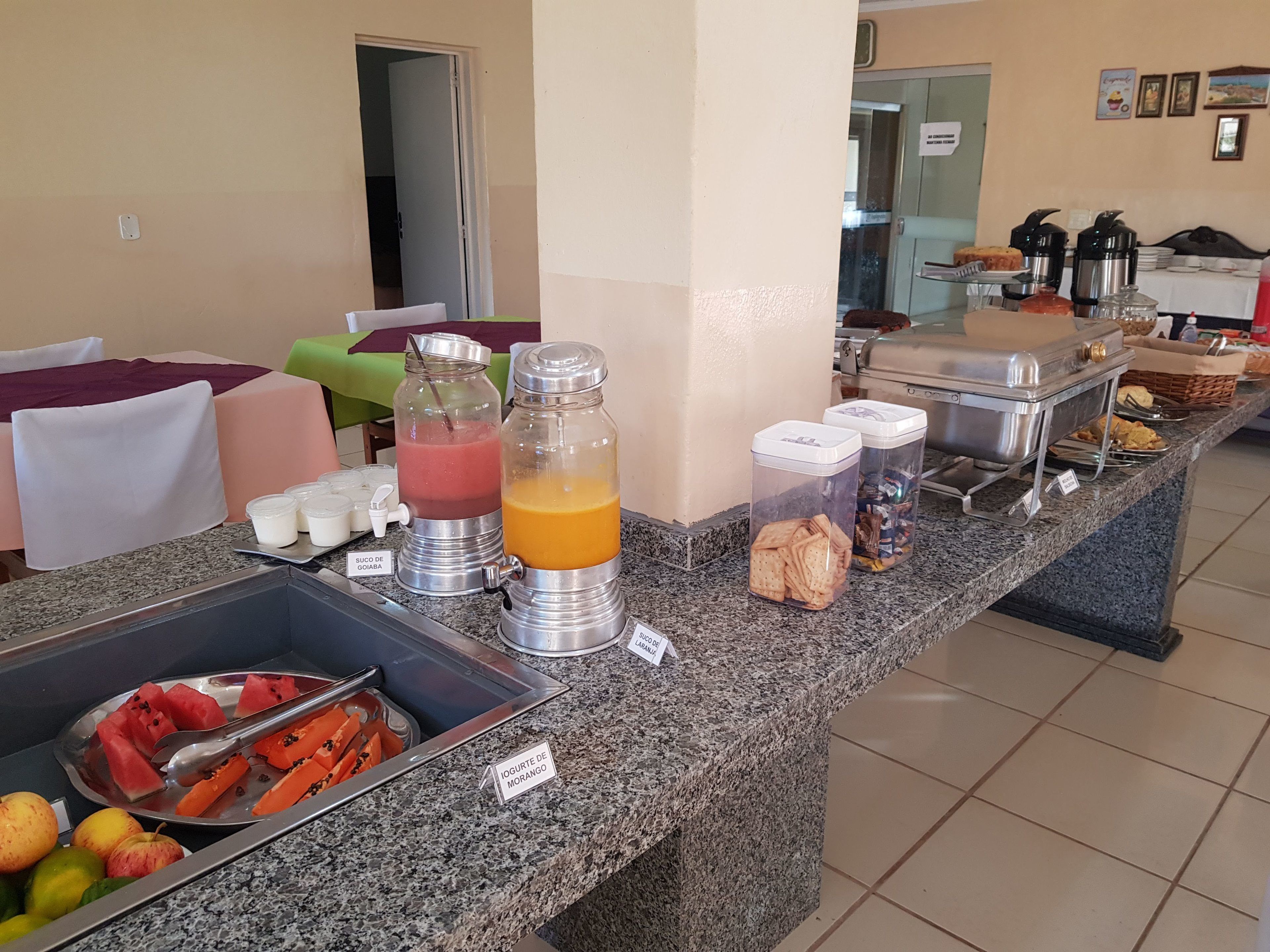Zona de bufé con diversos alimentos y bebidas, que incluye un bol de fruta, dispensadores de jugo y recipientes con bocadillos.