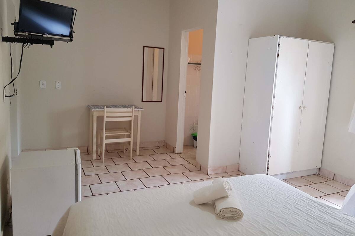 Une chambre à coucher avec un lit, un bureau, une chaise, une armoire et un téléviseur fixé au mur.