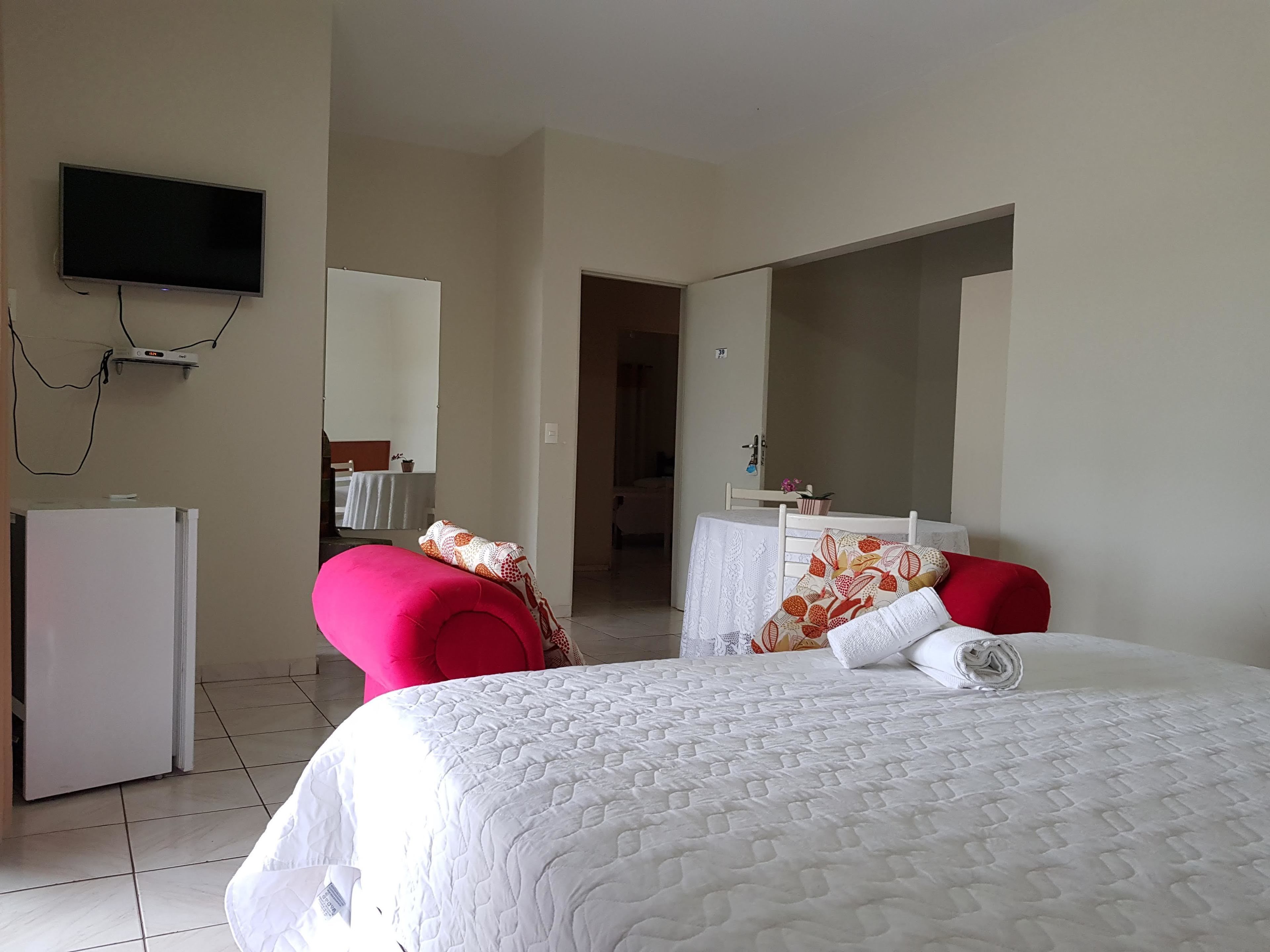 A hotel room with a bed, a TV mounted on the wall, a desk with a chair, and a bathroom visible through an open door.