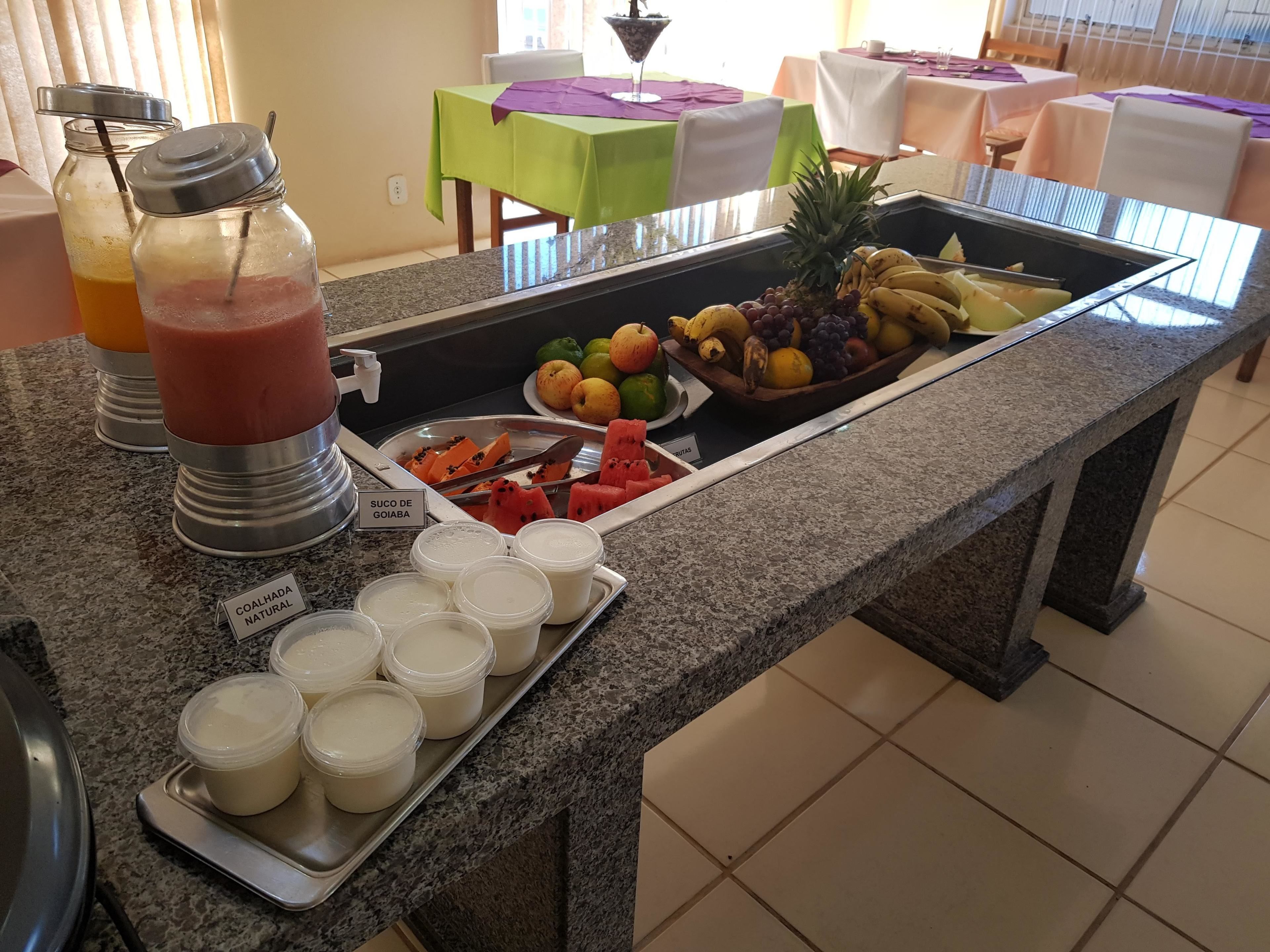Un bufé con diversos alimentos, incluyendo frutas, un plato de sandía y bebidas identificadas.