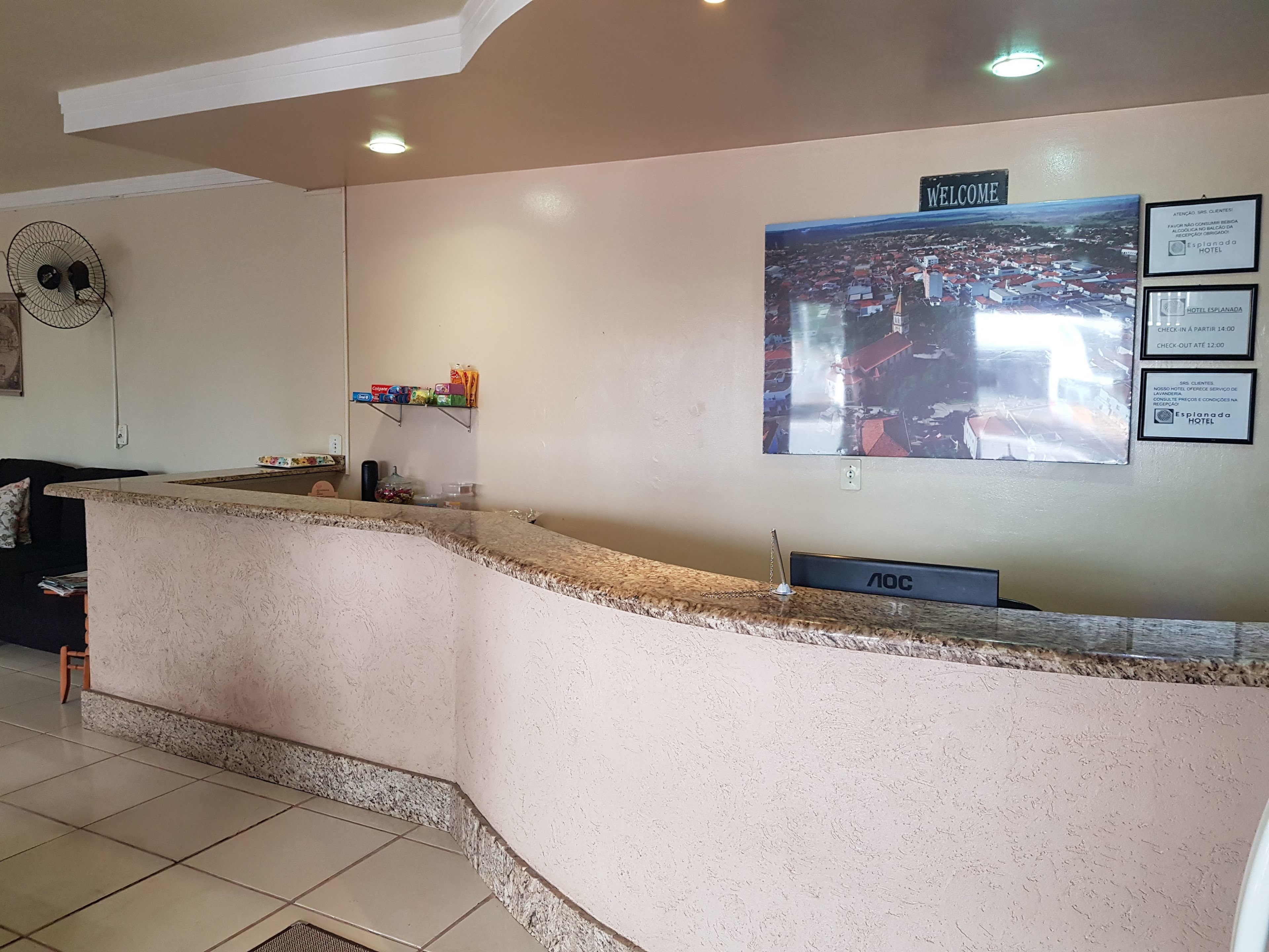 Zona de recepción de un hotel con mostrador, ventilador y cartel de bienvenida.