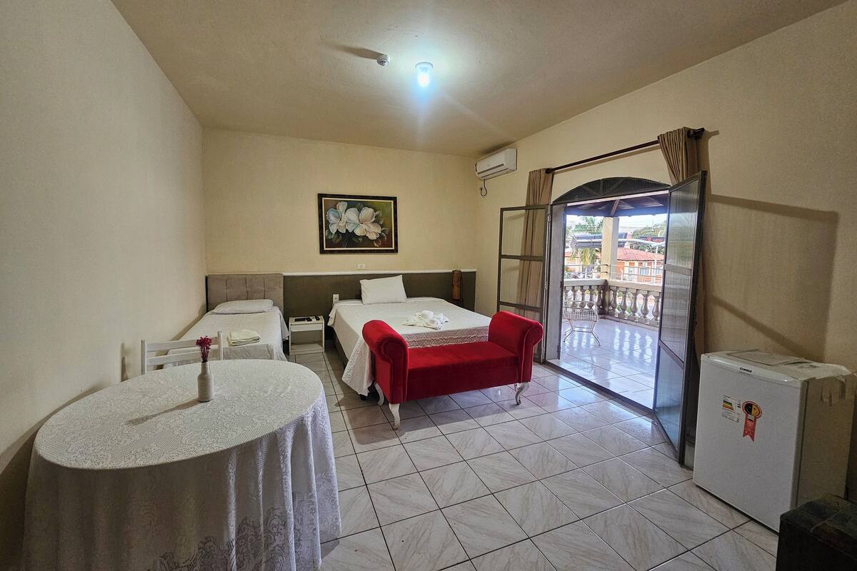 Une chambre d’hôtel avec deux lits, une petite table, une chaise rouge, un balcon avec vue et un réfrigérateur.