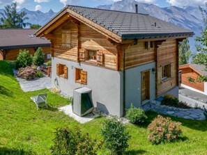 Un chalet en bois doté d’un toit à pente, d’un chemin de pierre et d’un jardin agrémenté d’arbustes et de fleurs.
