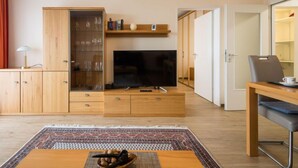 Ett modernt vardagsrum med en platt-TV, möbler i trä och en matplats med bord och stolar.