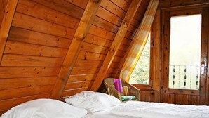 Ein Zimmer in einer Holzhütte mit einem Bett, einem Fenster und einem Sessel.