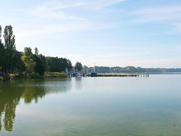 A calm lake with a dock and boats, surrounded by trees and a distant shoreline. - Nepumuk by Interhome (Arendsee)