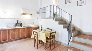 Una cocina con armarios de madera, una mesa de comedor con sillas, una escalera y un balcón pequeño.
