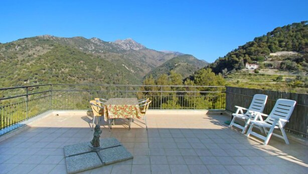 A terrace with a table and chairs, a statue, and a view of mountains.