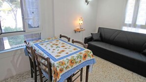 A dining area with a table covered in a floral tablecloth, a black sofa, and a wall-mounted lamp.