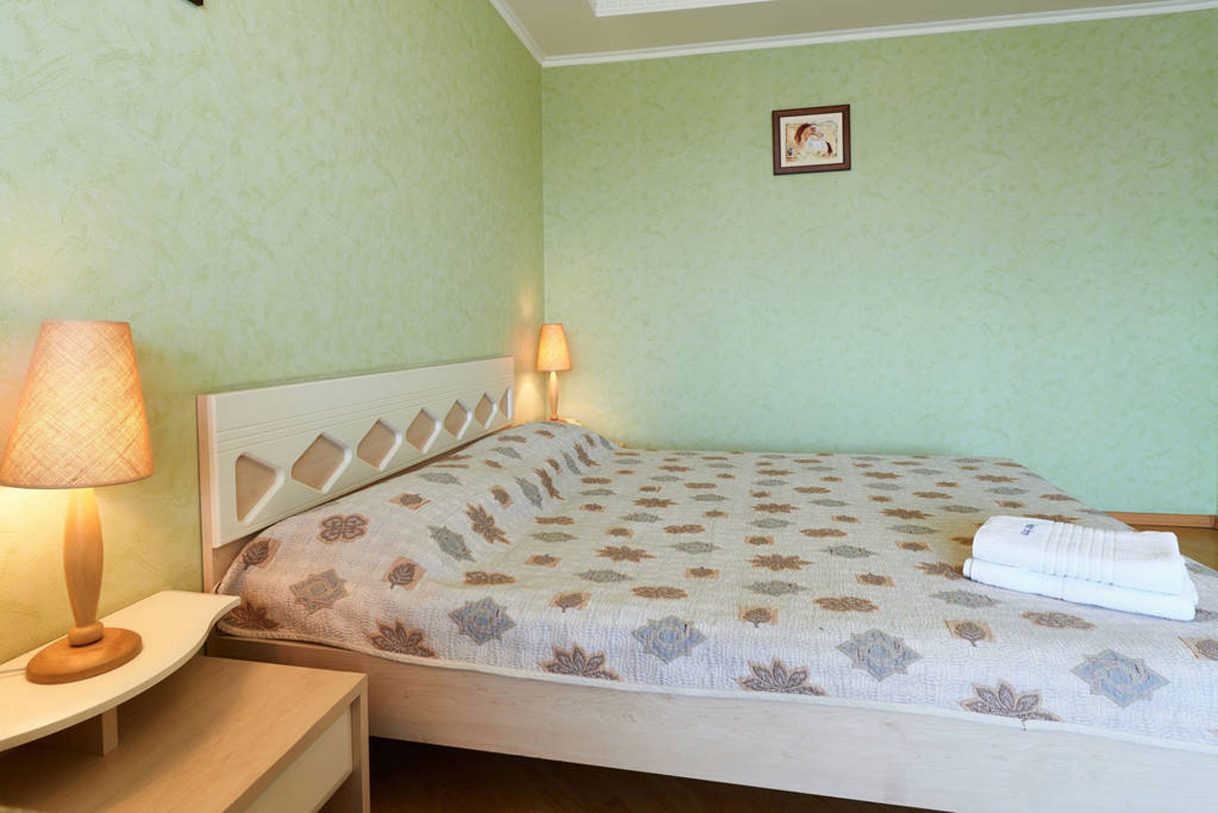 A bedroom with a bed, a nightstand, a lamp, and a wall-mounted picture.