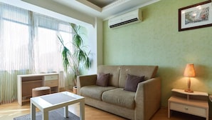 Ein Wohnzimmer mit einer Couch, einem kleinen Tisch, einer Lampe, einem Topf mit Pflanze und einer Wand-Klimaanlage.