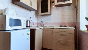 Eine kompakte Küche mit einer weißen Mikrowelle, einem kleinen Kühlschrank, Holzschränken und einer gefliesten Spritzschutzleiste.