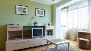 Ein Wohnzimmer mit Fernseher auf einem Schrank, einem kleinen Tisch und zwei gerahmten Bildern an der Wand.