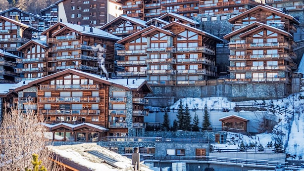 Un ensemble de chalets de montagne en bois, dotés de nombreux balcons, se dressant sur un fond de montagnes enneigées.