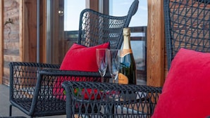 Des chaises en osier avec des coussins rouges sur un balcon, accompagnées d’une bouteille de champagne et d’un verre.