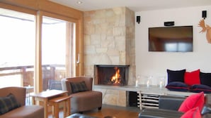 Un salon chaleureux avec une cheminée en pierre, des fauteuils confortables et un téléviseur à écran plat fixé au mur.