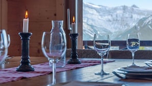 Une table à manger dressée avec des bougies, des verres à vin et des assiettes, avec une vue sur les montagnes en arrière-plan.