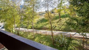 A view from a balcony overlooking a hillside with trees and a paved path. - Lunik Orion by Interhome (Le Corbier)