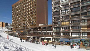 A multi-story hotel with a modern architectural design, featuring balconies and a ski slope in the foreground. - Apartment Ariane by Interhome (Le Corbier)