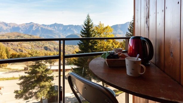 A balcony with a table, a chair, a red kettle, a mug, and a bowl of fruit. - Apartment Ariane by Interhome (Le Corbier)