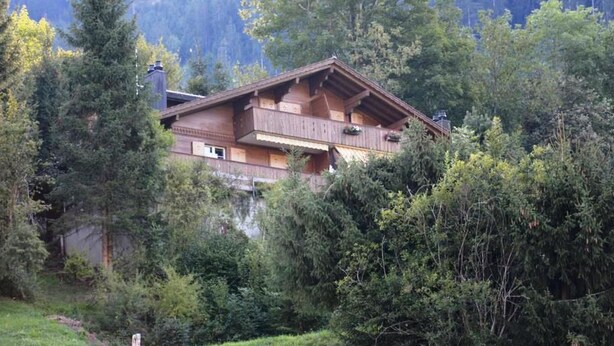 Un bâtiment de style chalet, entouré d’une forêt dense, doté d’un toit à forte pente et de balcons en bois.