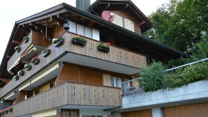 Un immeuble à plusieurs étages doté de balcons en bois, de jardinières et d’un télésiège visible sur le toit.