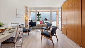 Zona pranzo moderna con tavolo in legno, sedie e vista sulle montagne attraverso ampie finestre.