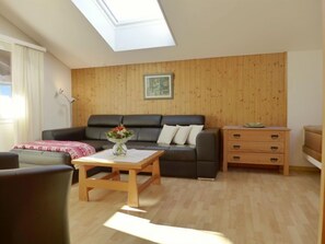 Una sala de estar con un sofá negro, una mesa de centro de madera con un florero, un aparador de madera y un tragaluz.