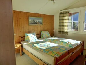 Un dormitorio con una cama litera de madera, una mesita de noche pequeña, un cuadro en la pared y una ventana con cortinas.