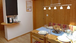 A wooden-paneled room with a dining table set for four, a small kitchen area with a toaster, and a wall-mounted TV. - Oltschiblick by Interhome (Brienzwiler)