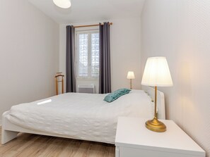 Een slaapkamer met een bed, bedlampen, een raam met gordijnen en een radiator.
