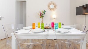 A dining area with a white table, clear chairs, colorful glass candle holders, and a wall-mounted TV.