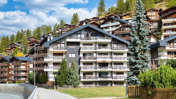A multi-story hotel with balconies, a pool, and a mountainous backdrop. - Residence A by Interhome (Zermatt)