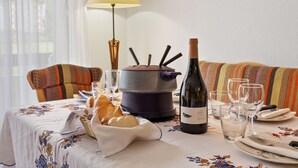 A dining table set with a bottle of wine, glasses, a bread basket, and a pot on a floral tablecloth. - Residence A by Interhome (Zermatt)