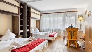 A hotel room with two beds, a wooden chair, a table with a lamp, and a view of the outdoors through sheer curtains. - Residence A by Interhome (Zermatt)