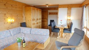 A cozy room with a wooden interior, a sofa, a dining table with chairs, and a small table with a bottle and glasses. - Le Bristol A20 by Interhome (Villars)
