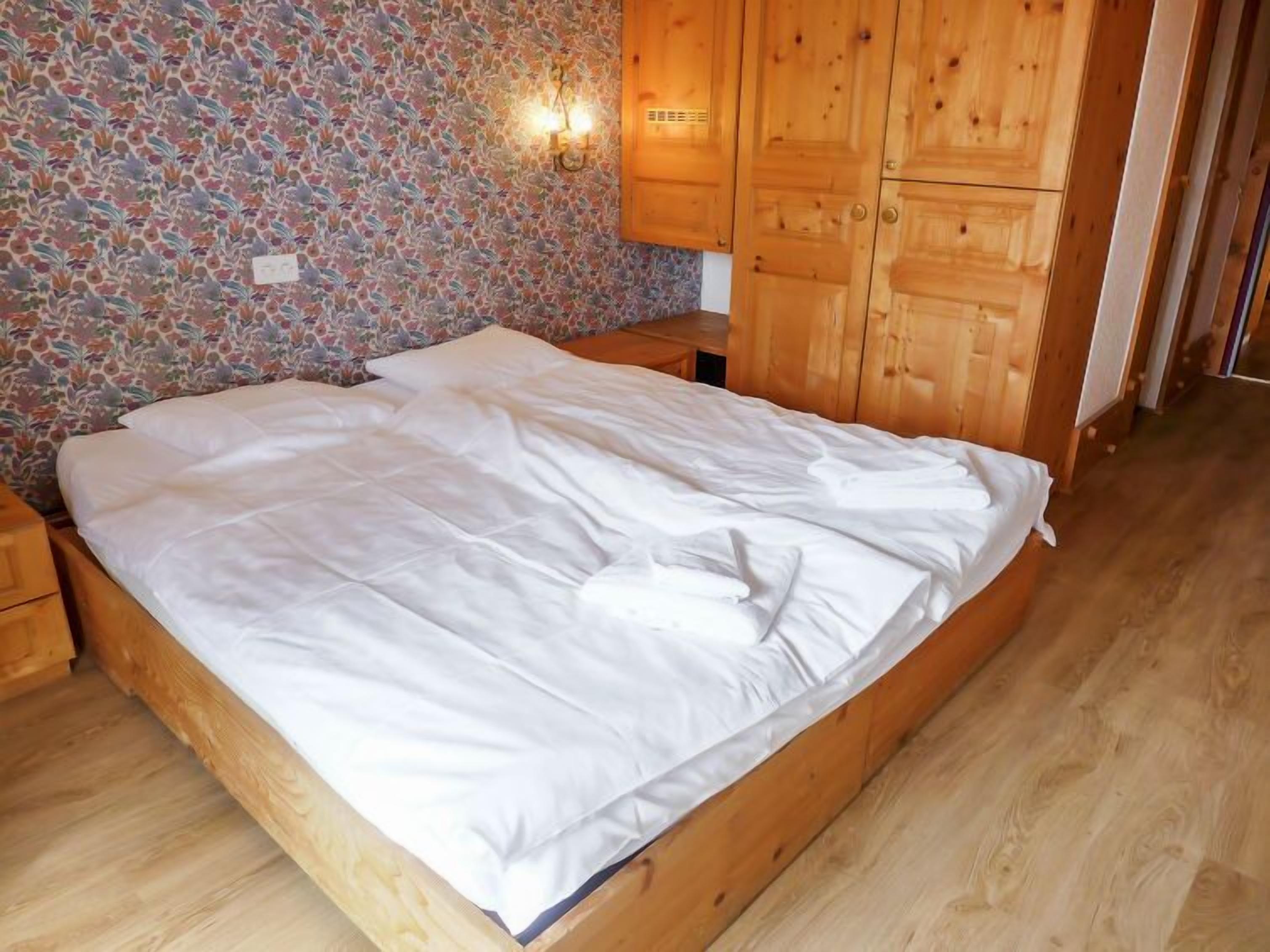 Una cama de madera con sábanas blancas en una habitación con pared de estampado floral y armarios de madera.