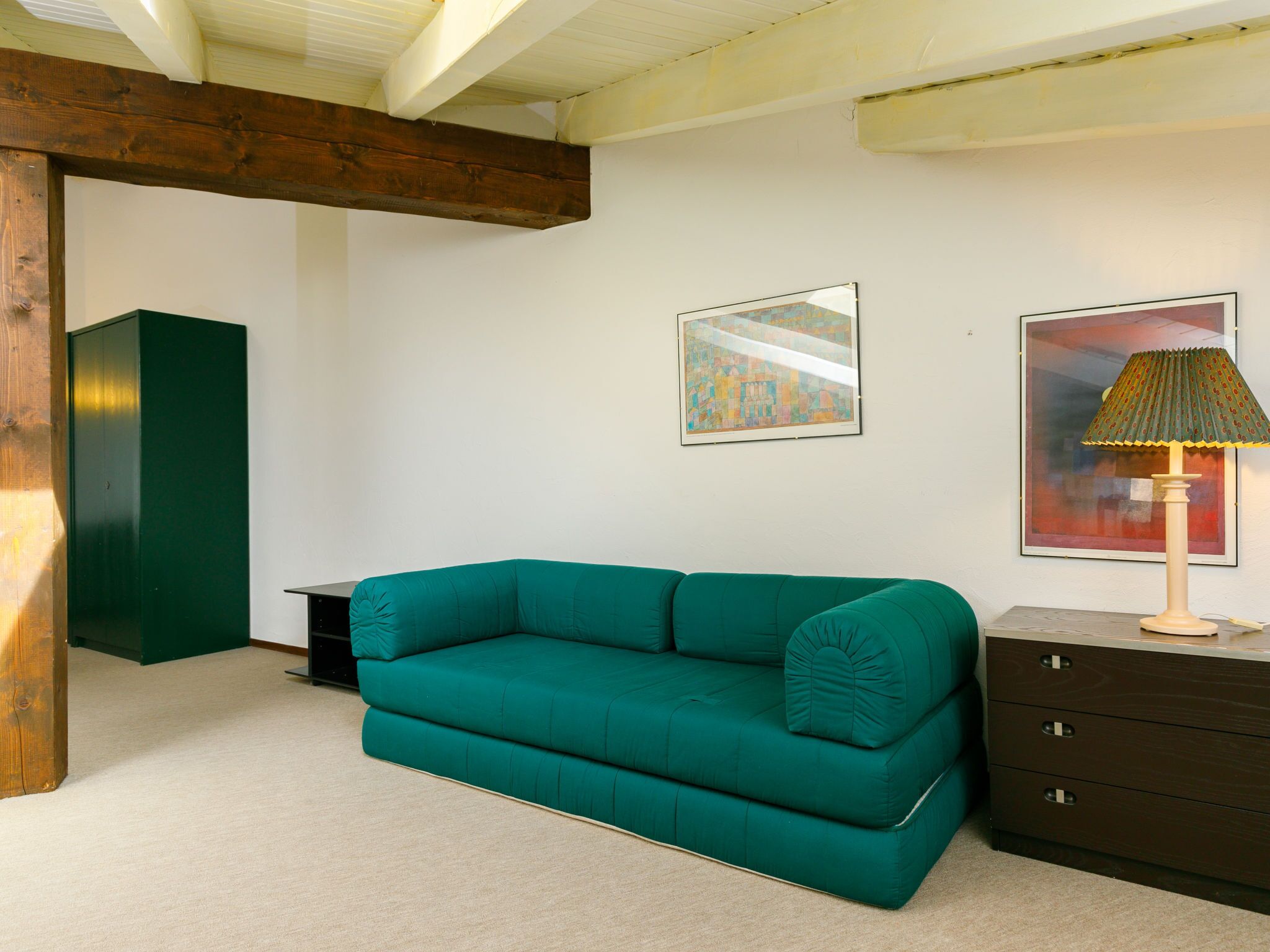 Un canapé de couleur turquoise dans une pièce aux murs blancs, avec un plafond orné de poutres en bois et un meuble vert.