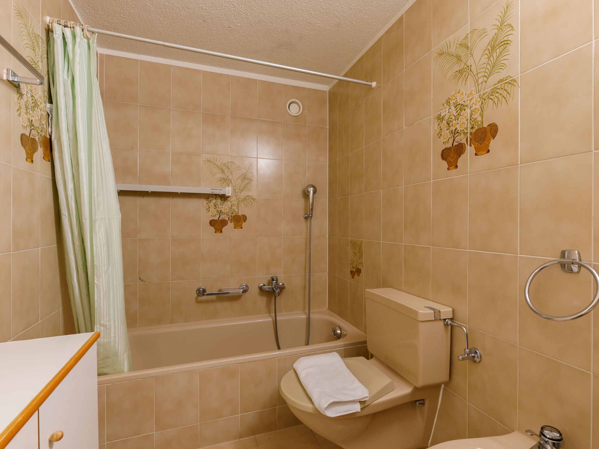 Une salle de bain avec des carreaux de couleur beige, une douche, des toilettes et un porte-serviettes.