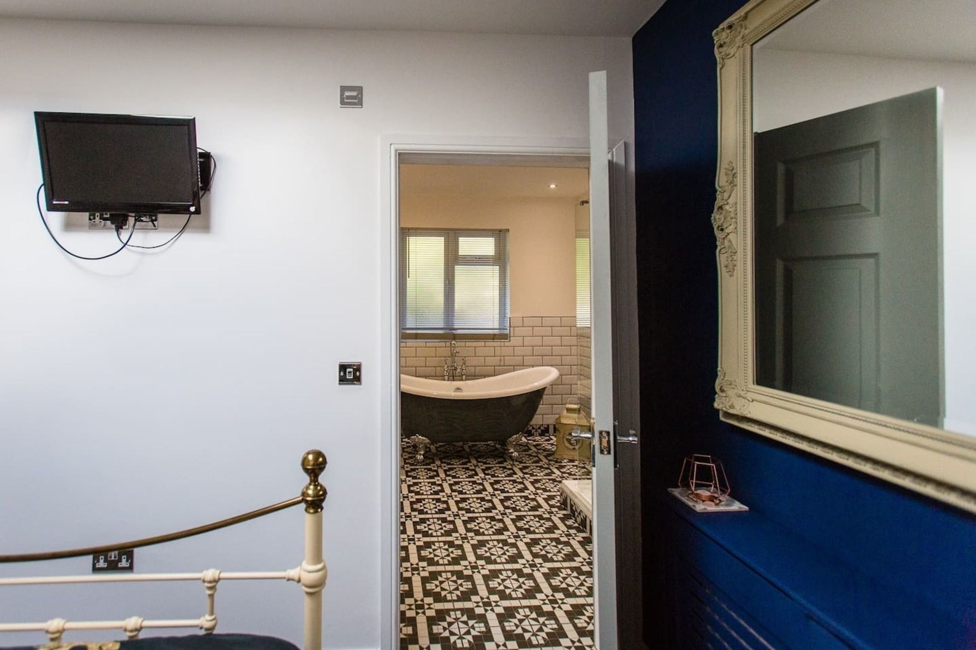 A bathroom with a bathtub, a toilet, and a sink. There is a television mounted on the wall and a door with a mirror.