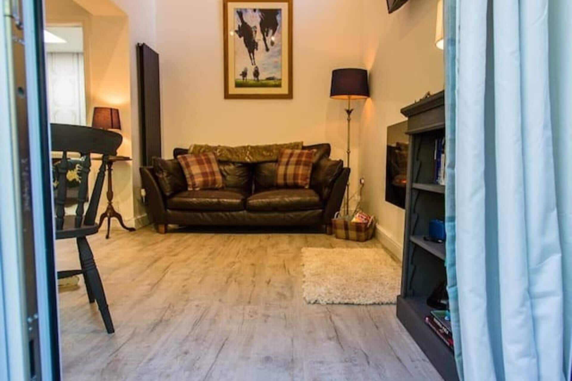 A living room with a brown leather sofa, a small rug, a framed picture on the wall, and a bookshelf.