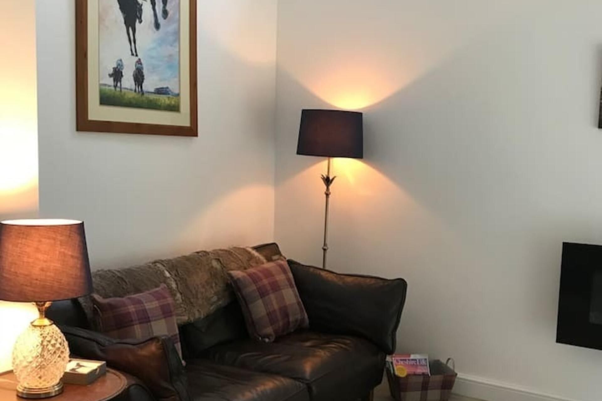 A living room with a brown leather sofa, a plaid throw pillow, a floor lamp, and a framed picture on the wall.