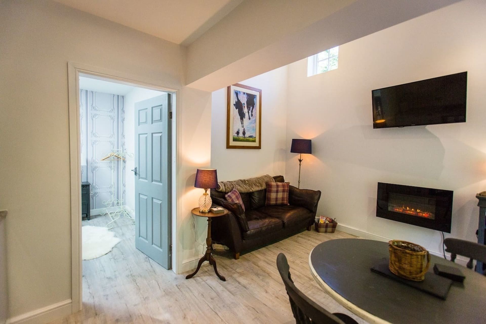 Een woonkamer met een open haard, een bank, een salontafel en een aan de muur bevestigde televisie.