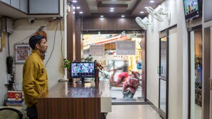 Un mostrador de recepción con un monitor de computadora mostrando varias cámaras de seguridad, un florero con flores y una moto roja afuera.